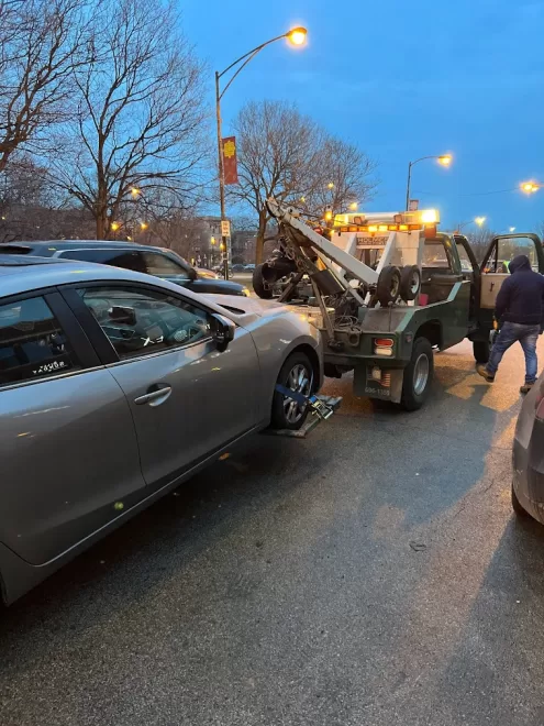 Reliable tow truck actively towing a vehicle with flashing lights on a busy road in Lakeview, Chicago, showcasing professional roadside assistance services.