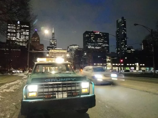 24/7 tow truck service in downtown Chicago, parked on the side of the road at night after offloading a vehicle, ready for another roadside assistance call.