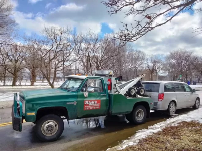 Springtime towing service in Chicago, loading a minivan from the rear tires amid melting snow and puddles under clear skies, showcasing our efficient emergency roadside assistance.