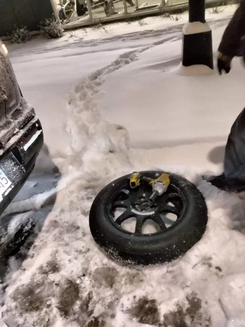 Emergency tire service in Chicago during extremely cold weather, with snow tracks visible, a spare tire on the ground, and an impact gun ready for use.