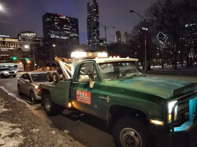 Emergency towing service by a tow truck in downtown Chicago during evening rush hour, highlighting our timely roadside assistance amidst heavy traffic.