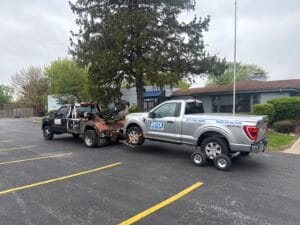 Commercial Ford F-150 work truck transported by wheel-lift tow truck and dollies to Rolling Meadows Illinois