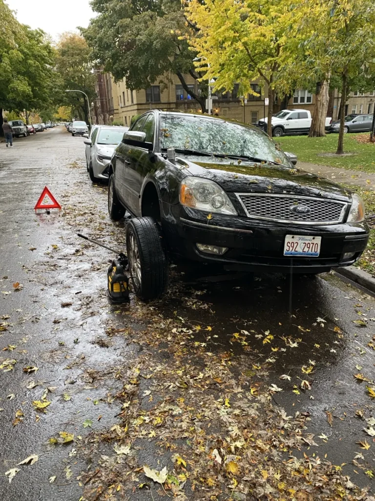 Black sedan floor jack on wet street.