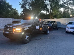 Black tow truck and dark vehicle at dusk.