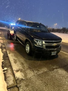 Black tow truck in falling snow at night.