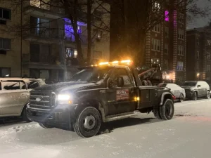 Black tow truck on snowy street at night.