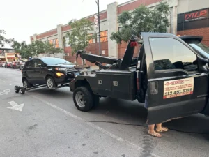 Black tow truck with dark sedan by storefronts.