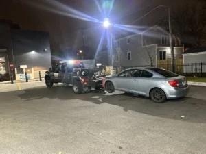 Black tow truck with silver sedan at night.