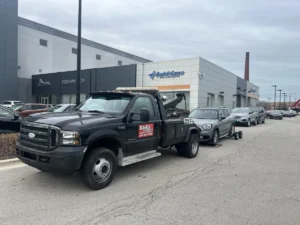 Black tow truck with silver suv at dealership.