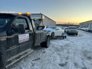 Black tow truck with white crossover in snow.
