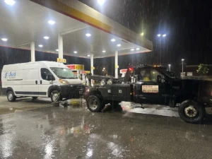 Black tow truck with white van in rain at night.