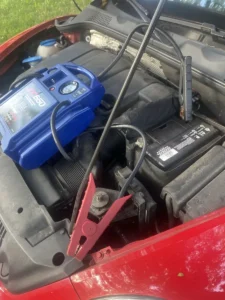 Blue jump starter in red vehicle engine bay.