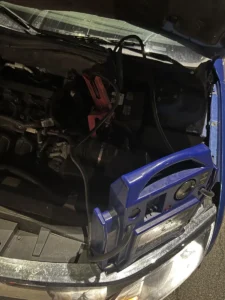 Blue portable jump starter under open hood.