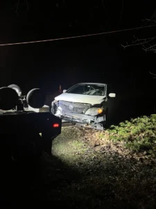 Damaged white car and tow equipment at night.