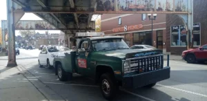 Green tow truck beneath elevated tracks.