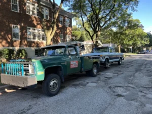 Green tow truck with blue pickup on residential street.