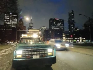 Green tow truck with city skyline at night.