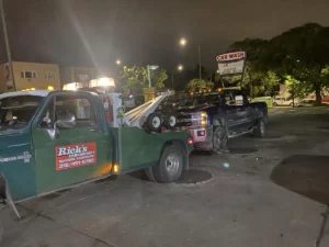 Green tow truck with dark pickup at night.