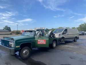 Green tow truck with gray passenger van.