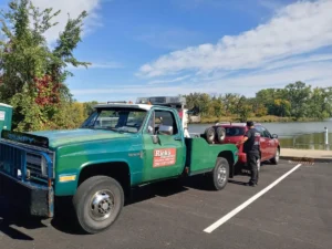 Green tow truck with red car in parking lot.