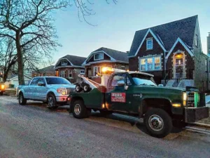 Green tow truck with silver suv residential street.