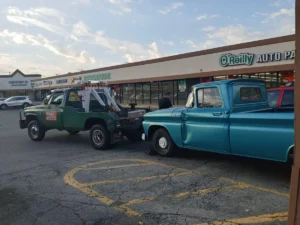 Green tow truck with vintage blue pickup.
