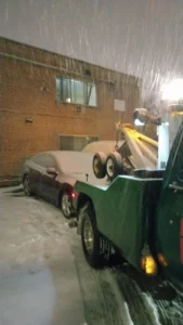 Green wheel lift truck in snow at night.