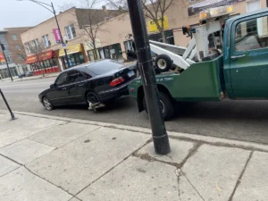 Green wheel lift truck with black sedan.