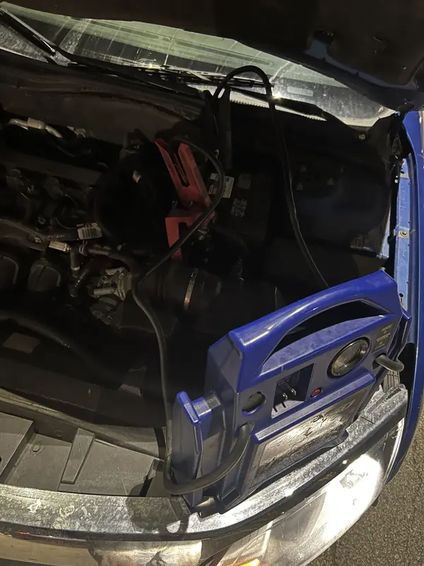 Portable battery jump starter connected under a vehicle hood.