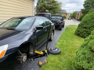 Dark sedan raised on a floor jack with a spare wheel beside it