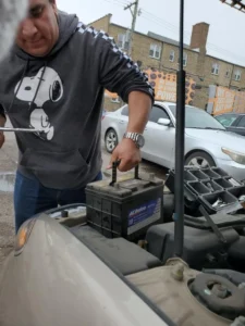 Technician handling car battery at engine bay.