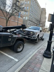 White pickup on wheel lift beside building.
