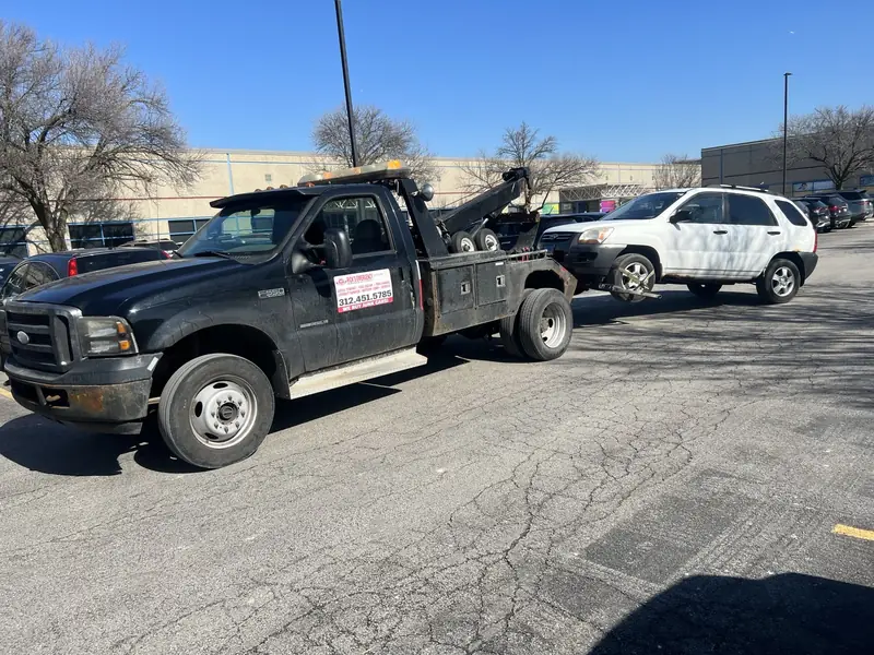 Rick’s black wheel-lift tow truck transporting a white SUV.